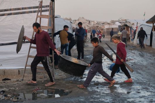 [자발리아=AP/뉴시스] 지난 7일(현지 시간) 가자지구 북부 자발리아 난민촌에서 한 남성과 아이들이 조리 기구를 들고 진흙탕이 된 통로를 지나고 있다. 2025.12.09.