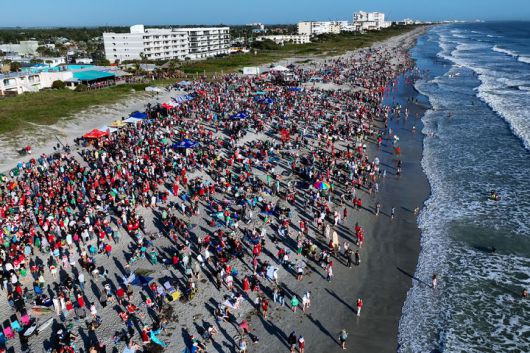 [코코아비치=AP/뉴시스] 24일(현지 시간) 미 플로리다주 코코아비치에서 크리스마스 이브를 맞아 열린 연례 ‘서핑 산타’ 행사에 산타 복장의 참가자들이 모여들고 있다. 2025.12.25.