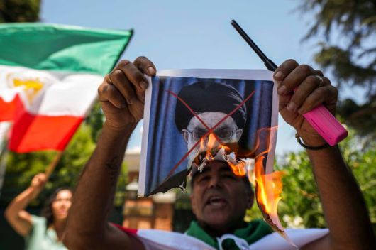 [산티아고=AP/뉴시스] 13일(현지 시간) 칠레 산티아고 주재 이란 대사관 밖에서 열린 이란 반정부 시위대에 연대하는 집회에 참석한 남성이 아야톨리 알리 하메네이 이란 최고지도자 사진을 태우고 있다. 2026.01.14.