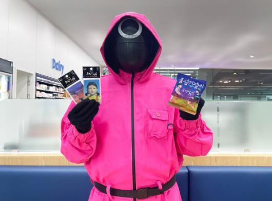 핑크솔져가 GS25에서 선보이는 오징어게임 시즌3 컬래버 상품을 들고 포즈를 취하고 있다. [사진=GS25]
