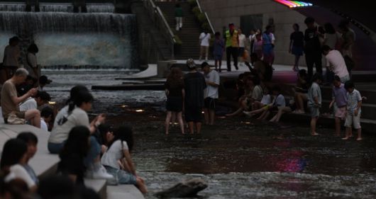 People cool off by Cheonggye Stream in downtown Seoul on the evening of July 6, 2025. Yonhap