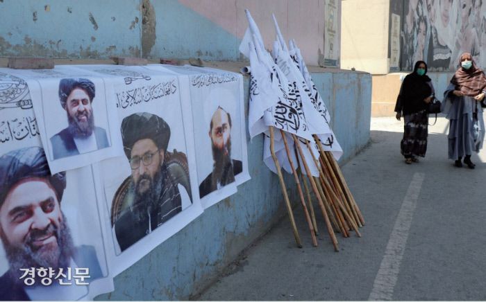 아프가니스탄 여성들이 8월 25일(현지시간) 수도 카불에 나붙은 탈레반 지도자들의 포스터와 깃발 옆을 지나가고 있다.  / AP연합뉴스