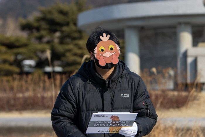 닭의 모습을 한 가면을 쓰고 나온 기본소득당 관계자가 좁은 닭장(케이지)에서 겪는 고통스런 삶을 호소하고 있다. 기본소득당 제공