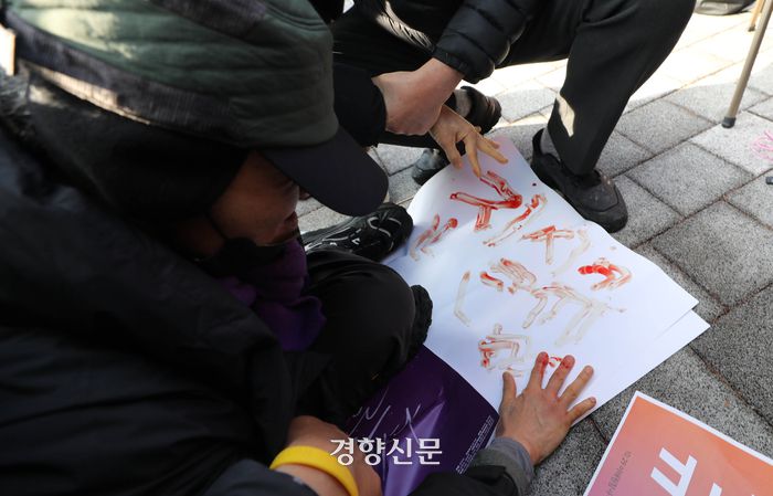 국민의힘이 이태원 참사 특별법에 대해 윤석열 대통령에게 재의요구권(거부권) 행사를 건의하기로 결정한 18일 서울 용산 대통령실 부근에서 이태원 참사 희생자 유가족 11명이 삭발식을 진행하는 중에 한 유가족이 혈서를 쓰고 있다.  김창길기자