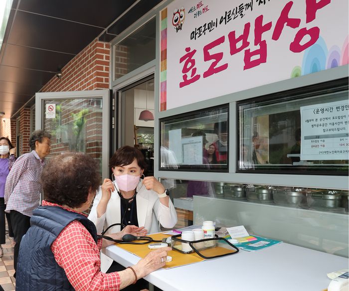 21일 효도밥상이 차려진 서울 마포구 망원2동 쌈지경로당 앞에서 마포보건소 직원이 식사 전 어르신들의 혈당과 혈압을 측정하고 있다. 마포구 제공