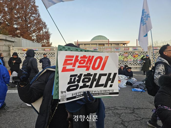 비상계엄이 해제된 4일 오전  한 시민이 서울 영등포구 국회 앞에서 ‘탄핵이 평화’라고 적힌 손팻말을 들고 있다. 김송이 기자