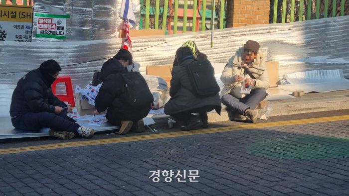 윤석열 대통령 탄핵 반대 집회 참가자들이 12일 오전 서울 한남초등학교 정문 옆 인도에 앉아 휴대용 태극기를 만들고 있다. 강한들 기자