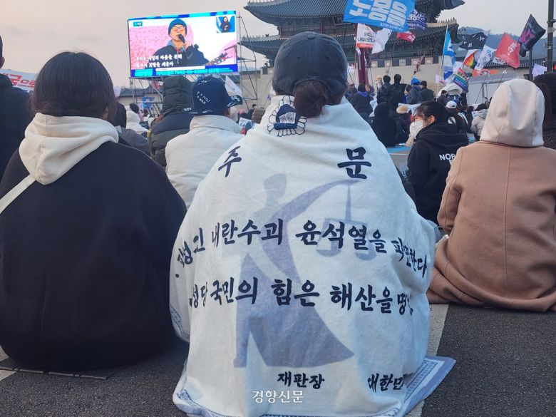 윤석열 대통령에 대한 탄핵을 촉구하는 집회 참가자가 8일 오후 서울 종로구 광화문 인근에서 ‘윤 대통령을 파면한다’는 내용 등이 적힌 담요를 덮고 앉아 있다. 우혜림 기자