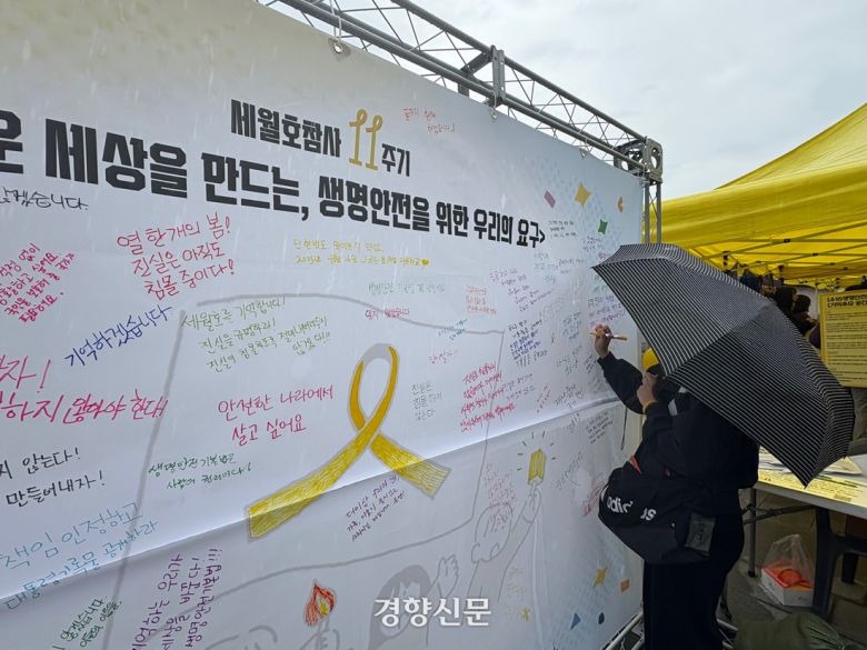 12일 오후 서울 종로구 경복궁 인근에서 열린 ‘세월호참사 11주기 기억·약속 시민대회’에서 한 시민이 ‘생명안전을 위한 우리의 요구’ 현수막에 글씨를 쓰고 있다. 배시은 기자