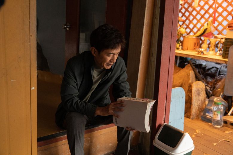 배우 안내상은 영화 <신명>에서 ‘열공TV’ 탐사보도 기자 정현수 PD를 연기했다. 그가 든 책면에는 ‘김석일(윤석열 전 대통령을 풍자한 캐릭터) 9수’라고 적혀 있다. 열공영화제작소 제공