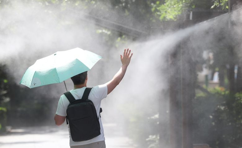 지난달 30일 대구 중구 국채보상운동기념공원에 쿨링포그(안개형 냉각수)가 가동 중인 가운데 한 시민이 양산을 들고 이동하고 있다. 연합뉴스 제공