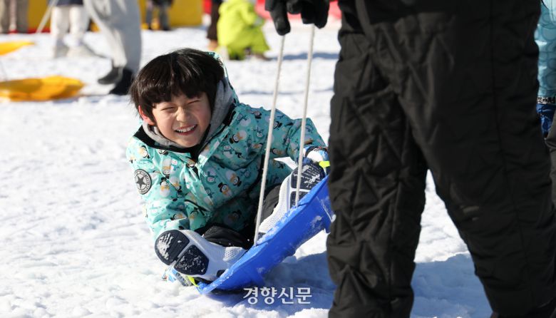 한 어린이가 아버지가 끌어주는 썰매를 타며 미소짓고 있다.