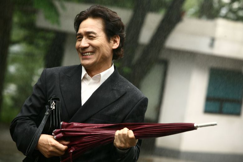 영화 <라디오스타>에서 매니저 박민수 역할을 맡은 배우 안성기가 우산을 들고 환하게 웃고 있다. 시네마서비스 제공