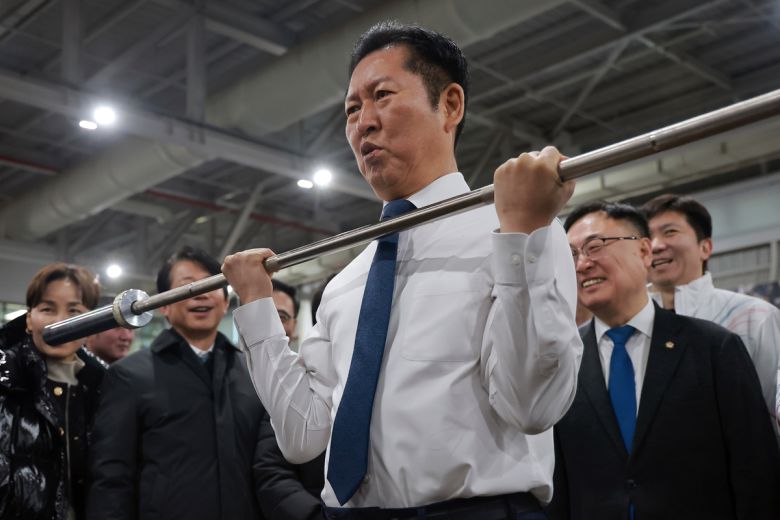 정청래 더불어민주당 대표가 23일 충북 진천 국가대표선수촌을 방문해 웨이트 트레이닝장에서 선수들을 격려하며 바벨을 들어보고 있다. 연합뉴스