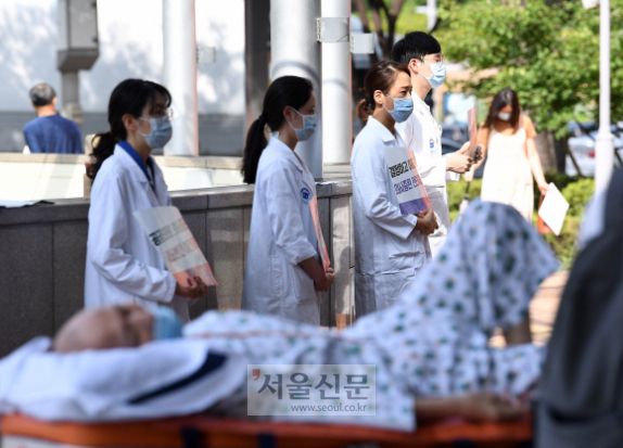 2차 전국 의사 총파업 첫날인 26일 서울 서초구 서울성모병원에서 이송되는 환자 뒤로 전공의들이 시위하고 있는 모습. 오장환 기자 5zzang@seoul.co.kr