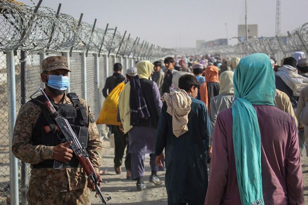 지난달 26일 아프가니스탄 피난민이 파키스탄 측이 국경 차만 검문소에 설치한 펜스를 따라 걷고 있다. 파키스탄 군인은 경계를 늦추지 않는 모습이다./AFP 연합뉴스
