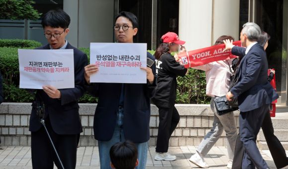 같은 장소 다른 마음 - 26일 서울 서초구 서울중앙지방법원 동관 앞에서 윤석열 전 대통령 재구속 촉구 의견서 제출 기자브리핑을 하는 참여연대, 군인권센터, 민주사회를 위한 변호사모임 회원들(왼쪽) 뒤로 윤 전 대통령의 지지자들이 손팻말을 펼치자 법원 관계자가 이를 제지하고 있다. 2025.5.26 연합뉴스