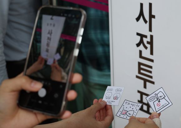 제21대 대통령선거 사전투표 첫날인 29일 서울 강남구 삼성2동주민센터에 마련된 사전투표소 앞에서 시민들이 투표 도장이 찍힌 그림을 들고 기념 촬영을 하고 있다. 2025.5.29 연합뉴스