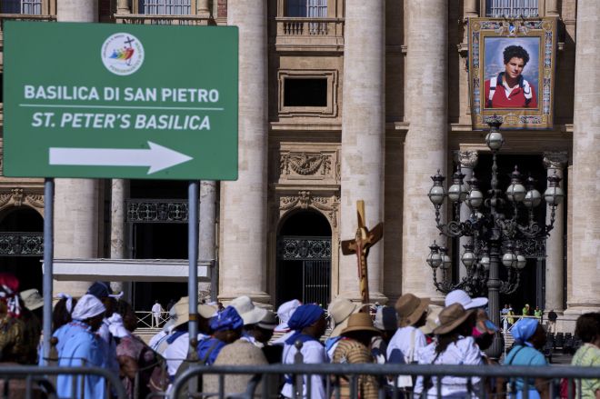7일(현지시간) 시성식을 앞두고 바티칸 성 베드로 대성당 외벽에 걸린 카를로 아쿠티스의 대형 태피스트리. 순례객들이 희년 행사에 맞춰 성문을 통과하고 있다. AP 연합뉴스