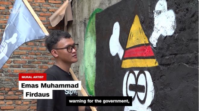 인도네시아 벽화가 에마스 무함마드 피르다우스가 ‘원피스’ 속 밀짚모자 해적단 깃발을 그린 졸리 로저 벽화를 완성하고 있다. 그는 ‘정부에 대한 경고의 상징’이라고 설명했다.  CNN 캡처