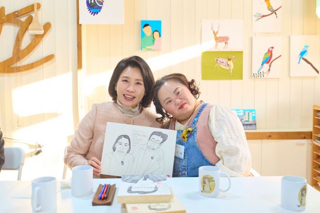 이재명 대통령 부인 김혜경 여사가 지난 3일 경기 양평의 ‘어메이징 아웃사이더 아트센터’에서 진행 중인 발달장애인 화가 겸 배우 정은혜 작가의 전시를 관람한 뒤 이 대통령 부부를 그린 작품을 한 손에 든 채 정 작가와 함께 기념촬영을 하고 있다. 뉴시스