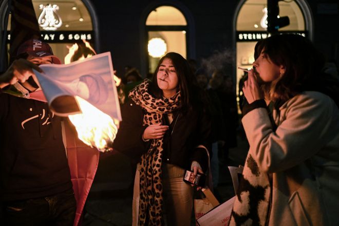 밀라노 미국 영사관 밖에서 반이란 정권 시위대가 이란 최고 지도자 알리 하메네이의 모습을 담은 불붙은 종이로 담배에 불을 붙이고 있다. 2026.1.14 AFP 연합뉴스