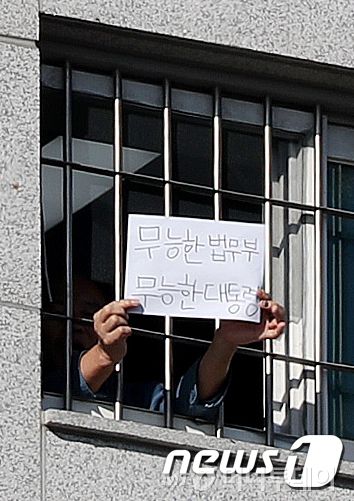 (서울=뉴스1) 민경석 기자 = 신종 코로나바이러스 감염증(코로나19) 집단 감염이 발생한 동부구치소가 발병 초기 117%에 달하는 과밀 수용 상태였던 것으로 조사됐다.  6일 오후 서울 송파구 동부구치소에서 한 재소자가 '무능한 법무부, 무능한 대통령'이라는 문구가 적힌 종이를 창살 너머로 꺼내 보이고 있다. 2021.1.6/뉴스1