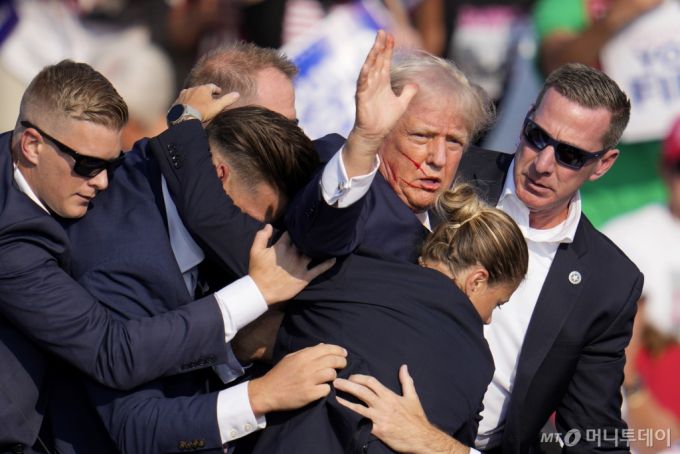 도널드 트럼프 전 미국 대통령이 13일(현지시각) 펜실베이니아주 버틀러에서 대선 유세 도중 암살시도 총격을 당한 직후 경호원들에게 둘러싸여 연단을 내려오면서 오른쪽 귀에 피를 흘리는 상태로 주먹을 흔들며 "싸우자"고 외치고 있다. 2024.07.14. /AP=뉴시스