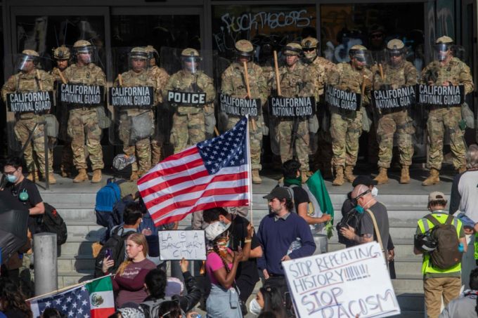 9일 로스앤젤레스에서 연방 이민 작전에 반대하는 시위대가 연방 건물 밖에서 경비를 서고 있는 캘리포니아 주방위군 대원들을 향해 피켓과 깃발을 들고 있다. /AFPBBNews=뉴스1