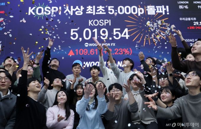 (서울=뉴스1) 오대일 기자 = 한국 증시가 사상 처음으로 '코스피 5000' 쾌거를 달성한 22일 서울 중구 우리은행 본점 딜링룸에서 직원들이 장중 최고가가 찍힌 전광판을 배경으로 코스피 5000 돌파를 축하하고 있다.   이날 코스피는 이재명 대통령이 '코스피 5000' 공약을 내걸고 임기를 시작한 지 7개월 만에 장중 꿈의 5000을 돌파하며 한국 자본시장의 역사를 새로 썼다. 2026.1.22/뉴스1  Copyright (C) 뉴스1. All rights reserved. 무단 전재 및 재배포,  AI학습 이용 금지. /사진=(서울=뉴스1) 오대일 기자