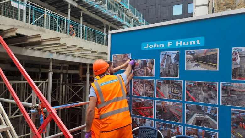 공사장 중간에 설치돼있는 파란 게시판에 붙어 있는 사진을 보고 토론 중인 현지 직원들. /백윤미 기자