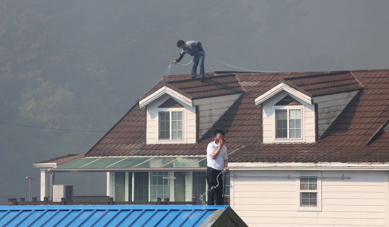 28일 오후 2시 1분쯤 대구 북구 노곡동 함지산에서 산불이 발생한 가운데 주민들이 주택 지붕에 물을 뿌리고 있다. /연합뉴스