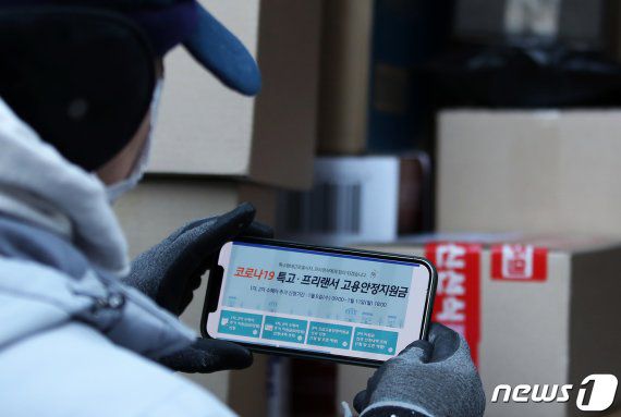 (서울=뉴스1) 오대일 기자 = 택배·퀵서비스 기사, 보험설계사 등 특수고용형태종사자(특고)와 프리랜서를 시작으로 본격적인 3차 긴급재난지원금 신청이 시작된 6일 서울 중구 충무로 인근 한 골목에서 한 택배 기사가 고용안정지원금 온라인 신청 사이트를 찾아보고 있다. 정부는 코로나19로 피해를 입은 특고·소상공인 등 580만명에게 50만~300만원씩 총 9조3000억원의 재난지원금을 지원한다. 거리두기 조치로 매출이 줄어든 소상공인에게는 최대 300만원의 버팀목자금을 지급하고, 특고·프리랜서에게는 최대 100만원의 고용안정지원금을 지원한다. 2021.1.6/뉴스1 /사진=뉴스1화상