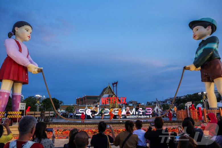 지난 30일(현지시간) 태국 방콩 시청 광장에서 열린 '오징어 게임 3' 홍보 행사에서 시민들이 줄넘기 게임을 하고 있다. 뉴스1                                    1일 오후 서울 종로구 광화문광장에 마련된 넷플릭스 시리즈 오징어게임 시즌3 팝업을 찾은 시민들이 드라마 조형물을 관람하고 있다. 뉴스1