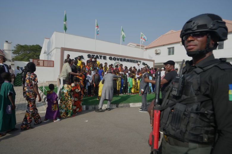 지난 22일(현지시간) 나이지리아 니제르주(州) 민나에서 풀려난 가톨릭 기숙학교 학생과 선생들이 정부 청사에 도착한 가운데 현지 경찰이 주변을 경계하고 있다. 지난 11월 21일 니제루 파피리의 세인트 메리 학교에서는 무장 괴한들이 시설을 습격해 학생 303명과 교사 12명 등 총 315명을 납치했다. 현지 당국은 군사 작전과 협상으로 21일까지 억류된 학생 전원을 구출했다.AP연합뉴스