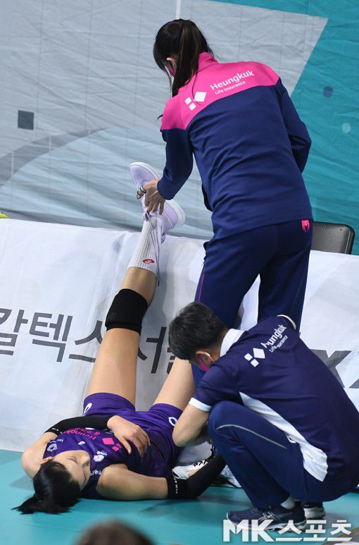 지친 김연경이 코트 위에 누운 채 광고판 위에 발을 올려놓자 김세영이 아픈 손으로 김연경의 신발끈을 풀고 있다.