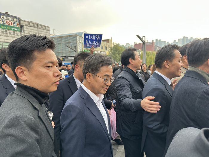 김동연 경기도지사가 이재명 더불어민주당 대표와 시장을 방문하다 인파 탓에 동선이 분리돼 뒤처져 걸어가고 있다. 한편 뒤에는 이재명 지지자의 ‘이재명 힘내라’ 피켓이 보인다. 2024.11.21 [구정근 기자]