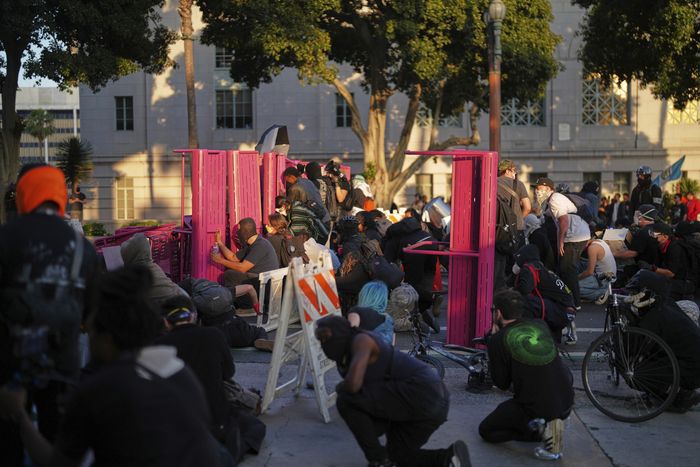 시위대가 전날 밤의 이민 단속 항의 시위에 이어, 2025년 6월 8일 일요일 로스앤젤레스 다운타운의 메트로폴리탄 구치소 근처에서 벤치 뒤에 몸을 숨기고 있다. [사진 = AP 연합뉴스]