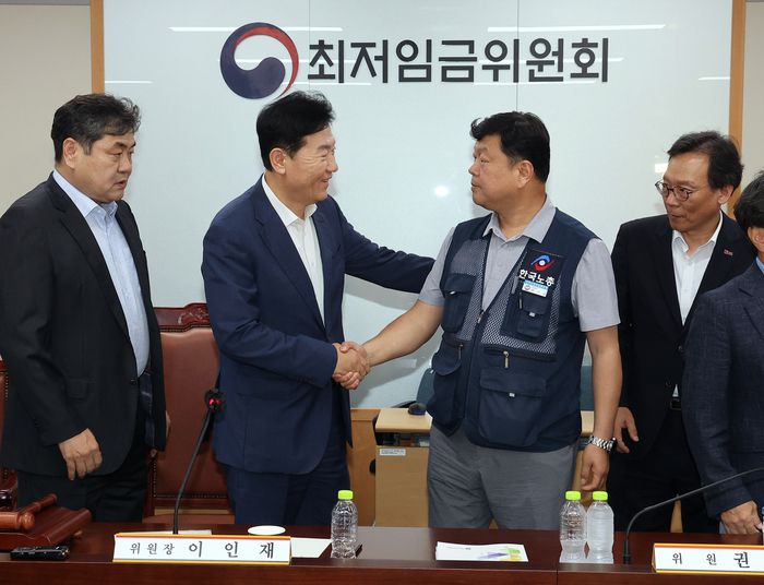 최저임금위원회 사용자위원 운영위원인 류기정 한국경영자총협회 전무(왼쪽 두 번째)와 근로자위원 운영위원인 류기섭 한국노총 사무총장(오른쪽 두 번째)이 10일 정부세종청사에서 열린 제12차 전원회의에서 내년 최저임금을 시간당 1만320원으로 17년만에 합의로 결정한 뒤 악수하고 있다. 왼쪽은 이인재 위원장. 2025.7.10 [연합뉴스]