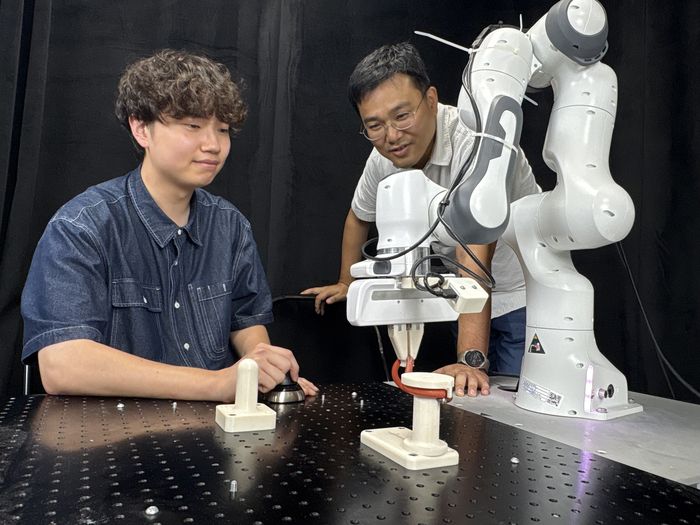 박대형 KAIST 전산학부 교수(오른쪽)와 논문 제1저자인 송민석 연구원이 로봇이 고무줄을 끼우는 모습을 보고 있다. [사진=KAIST]