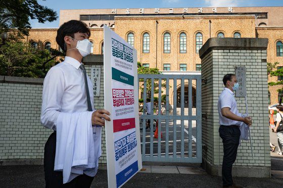 대한전임의협의회 소속 전임의들이 24일 서울 종로구 서울대 의과대학 입구에서 의사 가운을 벗어 들고 정부의 의과대학 정원 확대 등에 반대하는 손팻말을 들고 있다. 뉴스1