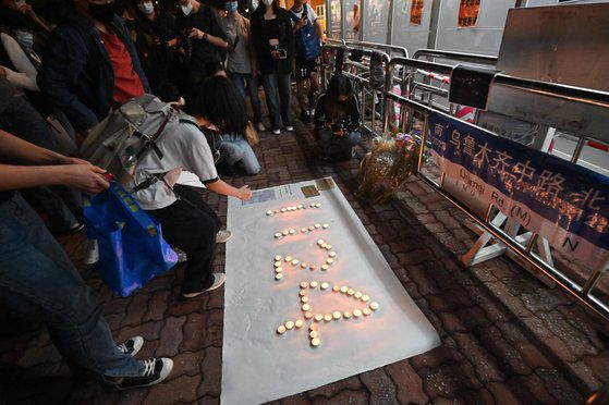 한 시위자가 28일(현지시간) 홍콩 중심가 센트럴에서 우루무치 화재의 희생자들을 추모하는 문구가 적힌 용지를 들고 있다. 그 옆에 서 있는 시위자는 A4 용지 백지를 들고 있다. AP=연합뉴스