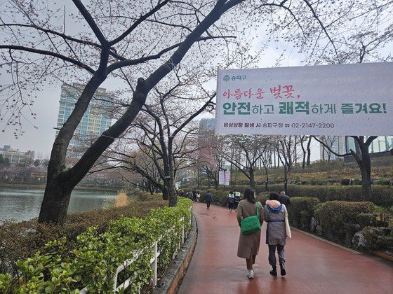서울 송파구 벚꽃축제 현수막 아래로 시민들이 지나가고 있다. 올해 송파구는 3월 27일부터 31일까지 벚꽃축제를 연다. 행사 사흘째인 29일 낮, 석촌호수를 찾았으나 아직까지도 대부분 벚나무는 개화하지 않은 모습이다. 신혜연 기자.