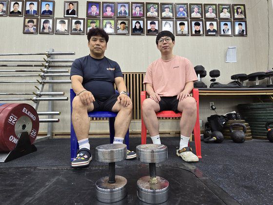 안산 선부중 역도부 조성현(50·왼쪽) 코치와 안산공고 역도부 박상민(32) 코치가 역도 여자 81㎏ 이상급 박혜정 등 역대 선부중 졸업 역도부원 사진이 걸려있는 벽면을 뒤로 하고 포즈를 취하고 있다. 손성배 기자