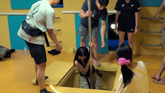 숙박객끼리 도와야 살 수 있는 '대환장 기안장'의 풍경. 봉을 버거워하는 한 숙박객을 주변에서 지켜보고 있다. 사진 넷플릭스