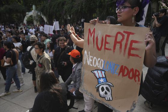 2025년 7월 4일 멕시코시티에서 미국인 유입으로 주택 가격이 오르자, 시위대가 젠트리피케이션에 반대하는 시위를 벌였다. 스페인어로 '신식민지 주민에게 죽음'이라는 글이 적힌 포스터. 미국 성조기를 연상케하는 모자와 해골 그림이 그려져 있다. AP=연합뉴스