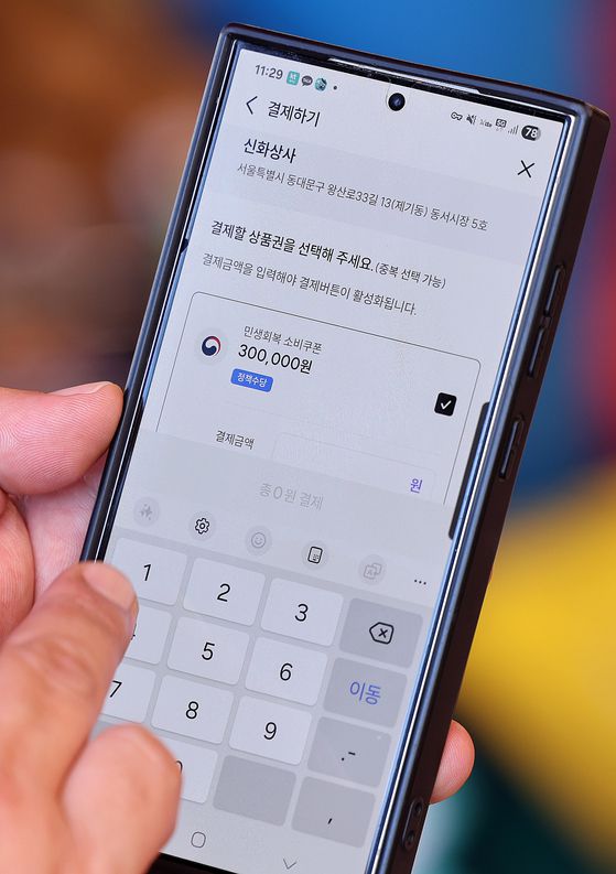 지난 27일 서울 동대문구 청량리종합시장을 찾은 한 시민이 소비쿠폰을 사용하고 있다. 뉴스1