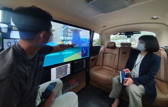 최정단 지능로보틱스연구본부장이 오토비에 탑승해 AR 실감가이드 기술이 적용된 OLED 디스플레이를 살펴보고 있다.