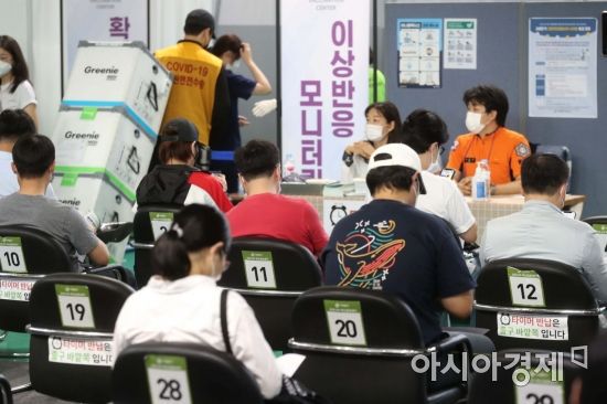 코로나19 확산세가 이어지고 있는 27일 서울 서대문구 북아현문화체육센터에 마련된 예방접종센터에서 백신을 맞은 시민들이 이상반응 모니터링 구역에서 대기하고 있다. 뒤편 관계자가 화이자 백신을 옮기고 있다. /문호남 기자 munonam@