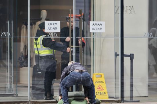 보안 요원들이 베이징 왕푸징 쇼핑 거리의 "태풍, 문 닫힘"이라고 적힌 표지판 근처에 자물쇠와 모래주머니가 달린 유리문을 단단히 고정하고 있다. AP연합뉴스